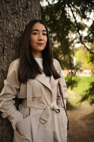 Woman in white shirt gazing downward among soft-focus spring greenery