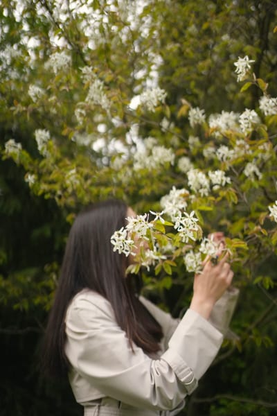 Woman in neutral coat against blooming white spring flowers and greenery