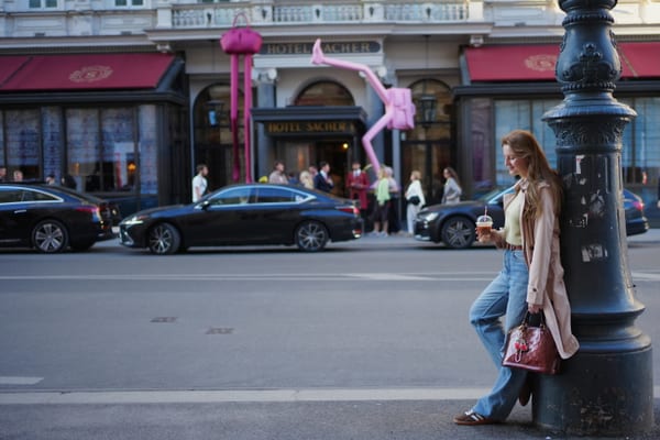 Woman leaning against an iron lamppost on a Vienna boulevard, Hotel Sacher and a pink street sculpture behind