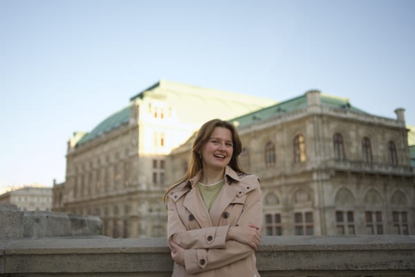 Woman laughing with arms crossed, the Vienna State Opera glowing behind her at dusk