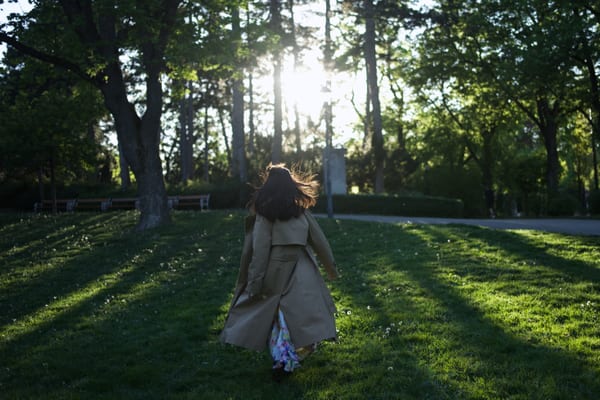 Woman walking away through Vienna park, hair flowing in motion, golden backlight