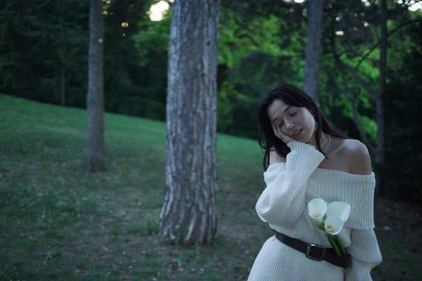 Woman in forest holding calla lilies with soft contemplative expression, Vienna park