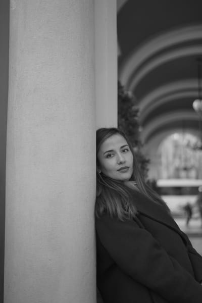 Portrait leaning against a stone column under arched arcades in Vienna