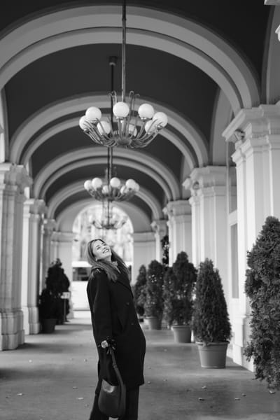 Woman laughing under a colonnade with chandeliers and potted trees in Vienna