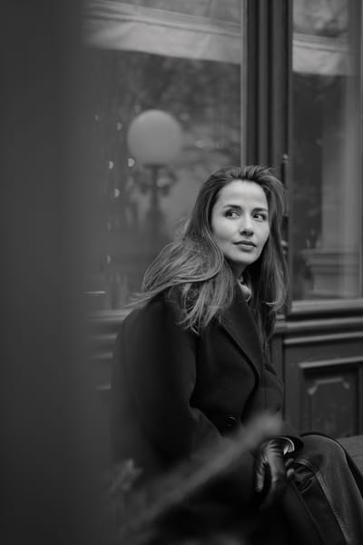 Black and white portrait seated outside a Vienna storefront, wind in her hair