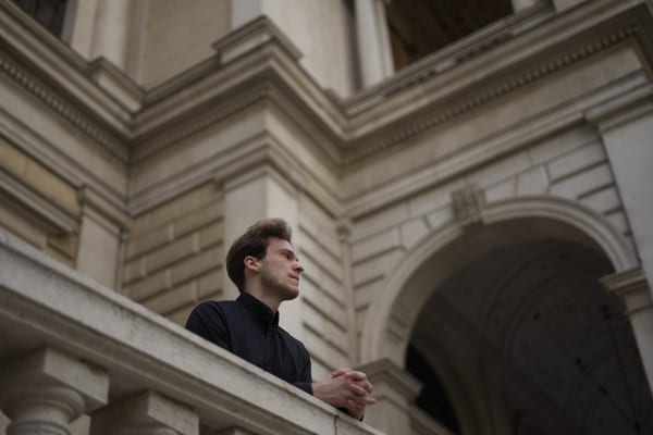 Man in a dark shirt leaning on a stone balustrade in the University of Vienna courtyard
