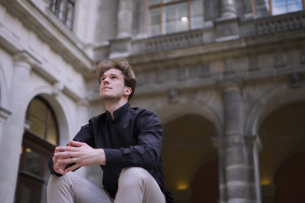 Man sitting with his hands folded, looking up at the arcades of the university courtyard