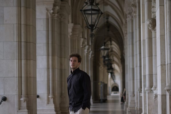 Man standing in the Gothic arcade of the Rathaus under a row of hanging lanterns